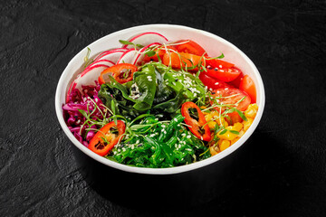 Colorful vegan poke bowl with corn, chuka seaweed, tomatoes and radishes