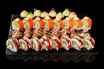 Delicious sushi rolls with salmon, sesame seeds, and various toppings arranged on black stone...