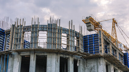 A frame made of load-bearing reinforced concrete walls during the construction of a multi-storey building. Reinforcement of reinforced concrete columns. A tower crane at a construction site.