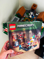 Naklejka premium Hand holding Minecraft Movie LEGO box in front of a setup with assembled LEGO models