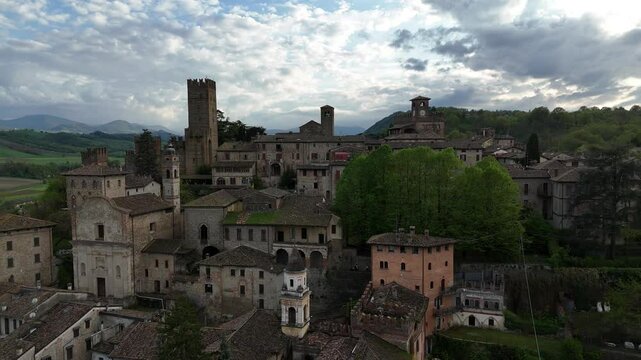 Drone view of Castell'Arquato medieval skyline showing Visconti Castle, clock tower and stone houses, surrounded by hills and woods, overcast spring sky, real time.