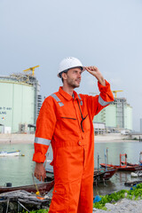 Worker in safety gear inspects industrial site near water with boats during overcast day