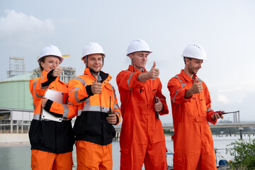Workers in safety gear show approval with thumbs up near a coastal construction site during daylight hours