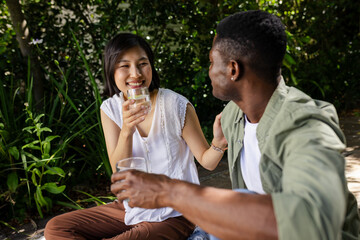 Smiling diverse couple having conversation in garden, with drinking glasses of water