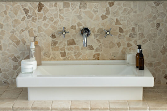 White sink basin is sitting on stone countertop, displaying chrome faucet and cosmetic bottles
