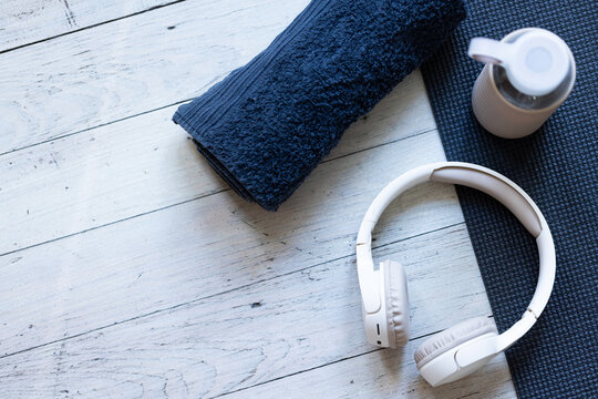 White wireless headphones are resting on dark textured yoga mat with rolled towel and water bottle