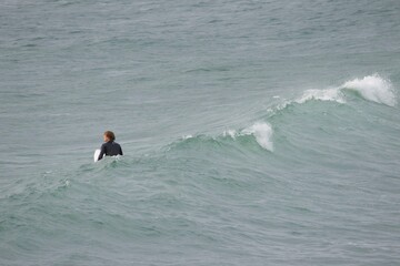 A surfer in a black wetsuit rides a breaking wave near the shoreline on a cloudy day. The powerful...