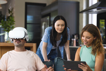 Using virtual reality headset, diverse friends sitting on sofa in living room, with tablet