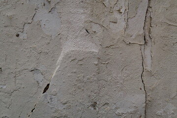 Mur granuleux enduit en blanc avec craquelures et fissures.