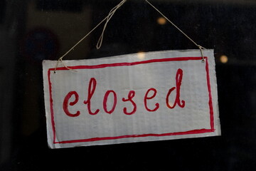 Closed (fermé) Panneau en carton avec inscription manuelle sur la porte vitrée d'un magasin.