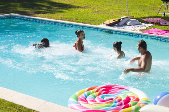 Splashing diverse friends chatting in backyard pool, with inflatable float and guitar - Powered by Adobe