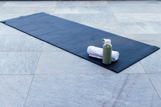 Exercise mat resting diagonally on stone terrace, showing rolled towel and green water bottle