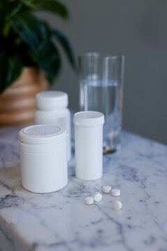 Medication bottles are standing on marble countertop, tablets lying near water glass and plant
