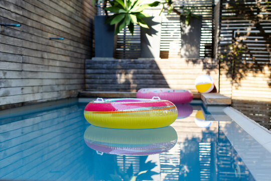 Yellow and pink inflatable ring floating in backyard pool with donut float, beach ball, planters - Powered by Adobe