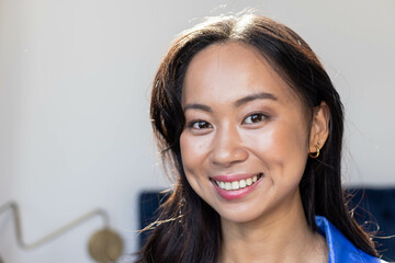 Smiling Chinese woman posing in living room, with curved gold-accent lamp and blue seat