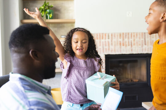 Diverse family sharing gift moment in living room, with wrapped gift box and greeting card