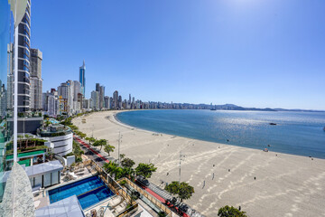 Aerial and elevated photos of the main beach in Balne&aacute;rio Cambori&uacute;, Santa Catarina, Brazil. The images show the coastal skyline with tall buildings, white sand, calm sea, and lush green mountains in t