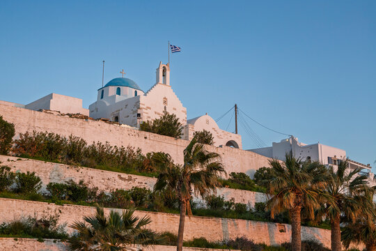 Traditional white and blue Agios Konstantinos (Saint Constantine) church on a hill in Paroikia (Parikia) town on Paros island in Greece under a clear blue sky at sunset. - Powered by Adobe