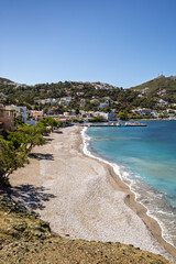 Fototapeta premium Scenic view of a beach and buildings along the hilly coast in the idyllic village of Myrties (Mirties) on Kalymnos island in Greece on a sunny day.