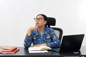 Female teacher in civil servant uniform with papers,books and laptop on the desk thinking...