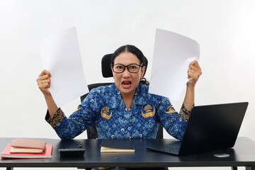 Stressed Female teacher in civil servant uniform with paper and laptop on the desk holding papers