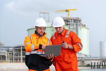 Construction workers collaborate on a laptop while inspecting a gas facility under a cloudy sky
