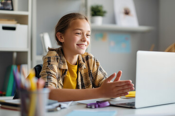 A girl smiling during a video call at a desk with a laptop, in a room