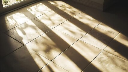 Warm golden sunlight creates bold windowpane shadows across a ceramic tiled floor in an indoor room setting filled with early morning or late afternoon ambiance