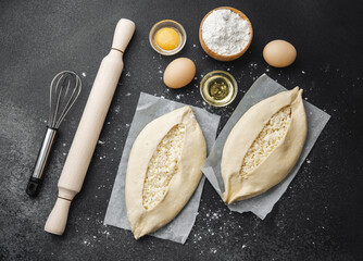 Top view of ingredients and two uncooked khachapuri on floured black table