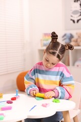 Motor skills development. Little girl playing with colorful dough at table indoors