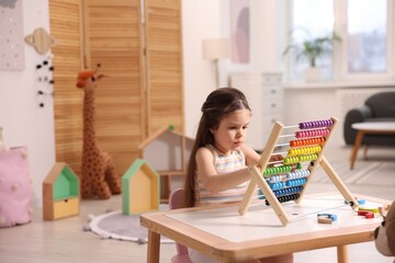 Motor skills development. Little girl playing with wooden abacus at table indoors, space for text