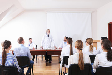 Senior doctor giving lecture near projection screen in conference room