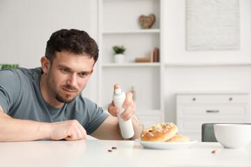 Emotional young man spraying insecticide onto pretzel with cockroaches at white table indoors. Pest...