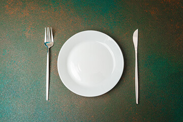 Simple table setting with fork and knife beside white plate on textured surface