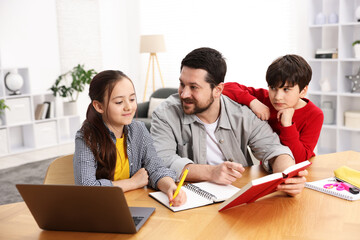 Father helping his kids with homework at wooden table indoors
