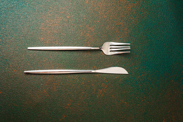 Silver fork and knife positioned on a textured green surface with rustic tones
