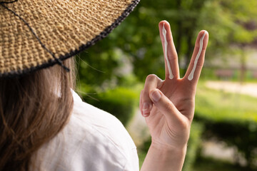 Closeup of a woman in a hat applying sufficient amount of sunscreen for the face and neck – two finger lengths.