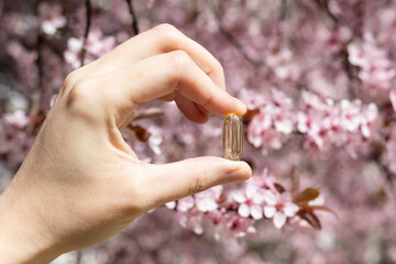 Closeup of a vitamin D capsule with cherry blossom in the background. Concept of supplementing vitamin D in spring. 