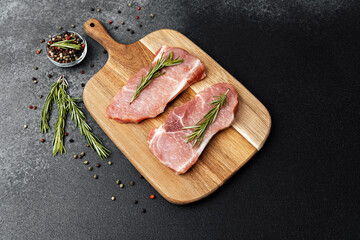 Fresh pork chops ready for cooking with herbs on wooden cutting board