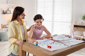 Fototapeta premium Girl and her mother drawing family tree with paints at wooden table indoors