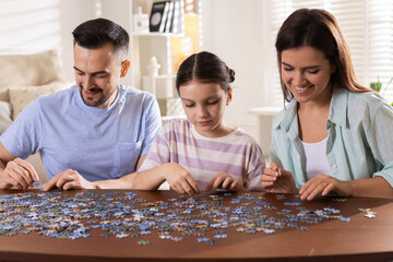 Happy parents and their daughter solving puzzle together at wooden table indoors