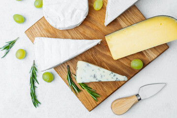 Cheese platter with assorted cheeses, grapes, and herbs on wooden board