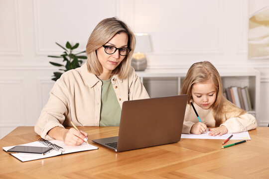 Single mother working and her daughter drawing at wooden table indoors