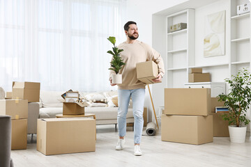 Moving day. Man with cardboard box and houseplant in his new home