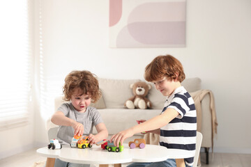 Cute little brothers playing with toys at table indoors