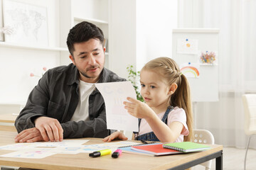 Teacher having lesson with little girl at desk indoors