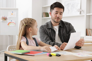 Teacher having lesson with little girl at desk indoors