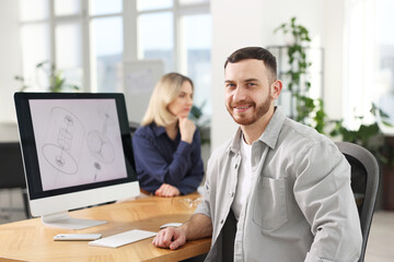 Smiling engineer and his colleague working with computers at table in office