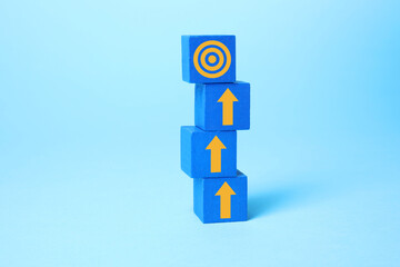 Targeting. Stacked cubes with arrows pointing at bullseye on top cube against light blue background