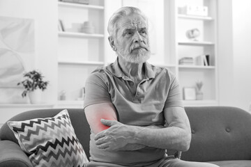 Arthritis. Senior man suffering from pain in elbow at home. Black and white toning with red color...